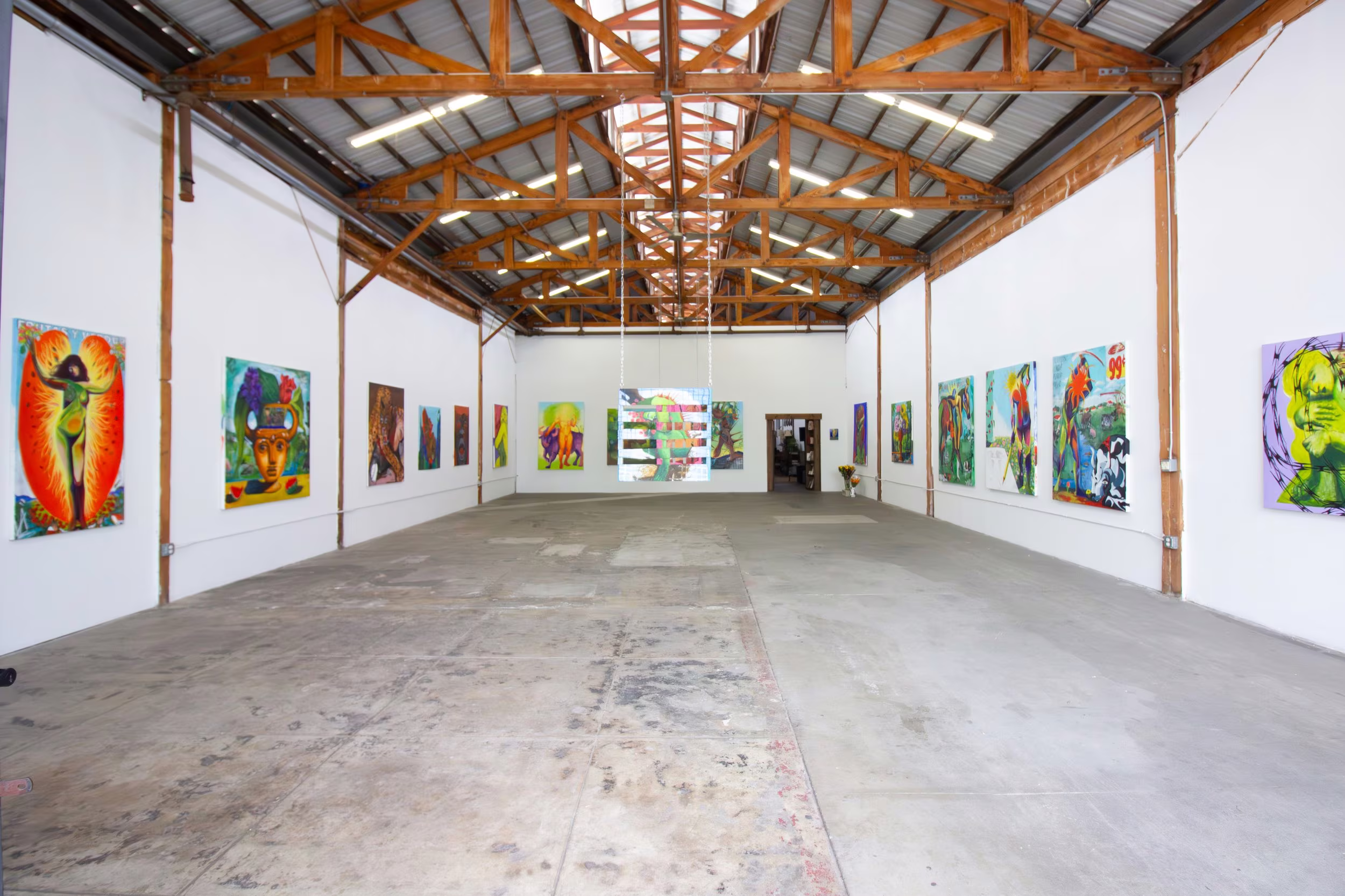 Long symmetrical gallery with bright figurative paintings along both walls beneath exposed wood trusses.