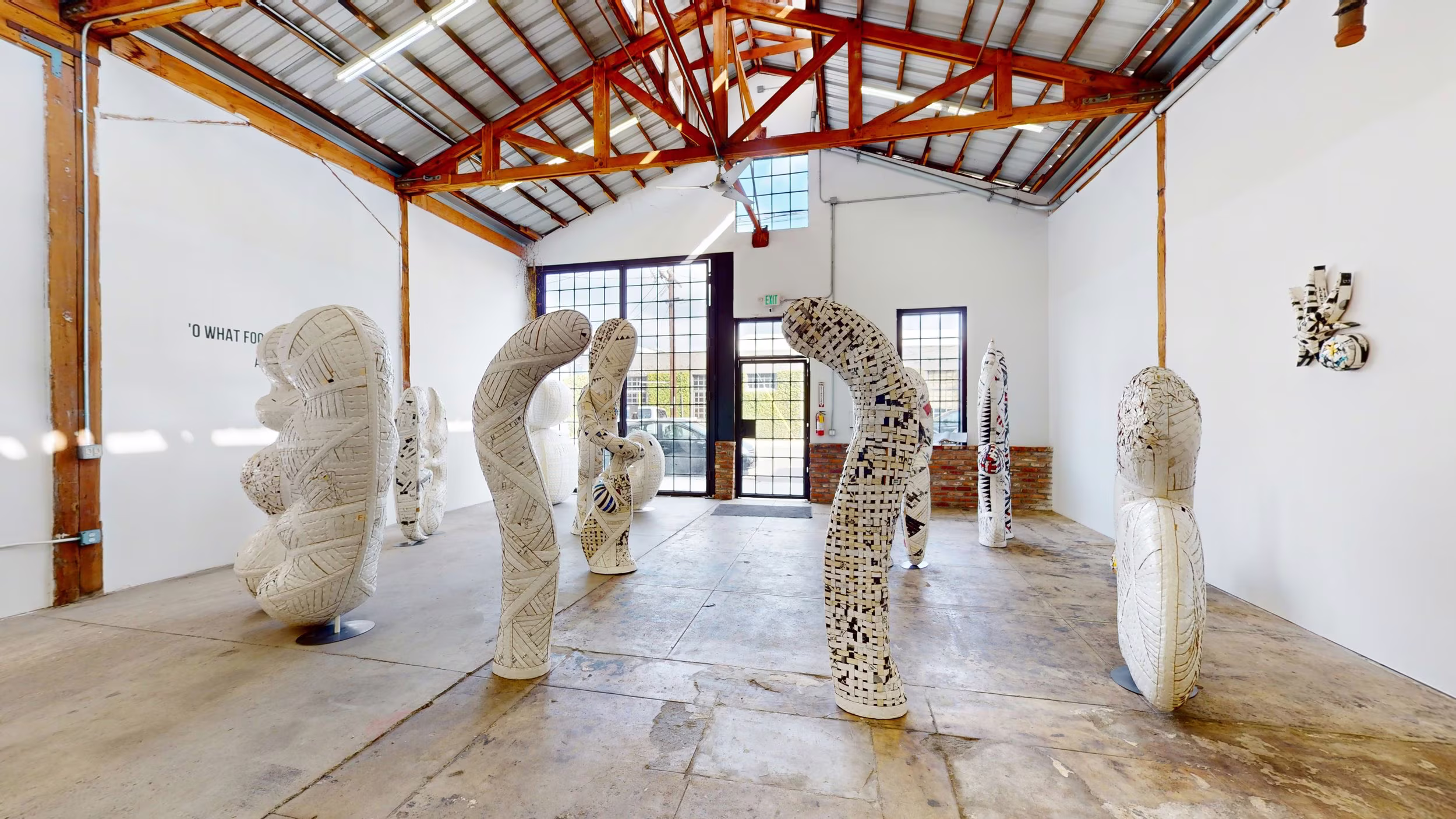 Walk-through arrangement of tall white woven sculptures leading toward gridded glass doors.