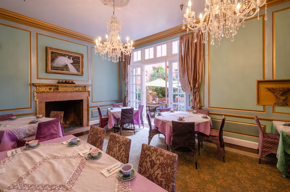Sunlit corner of the pastel tea room with fireplace, crystal chandeliers, lavender chairs, and garden doors.