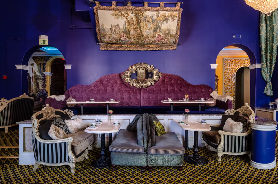 Long purple banquette and intimate table groupings beneath a tapestry in the blue dining room.