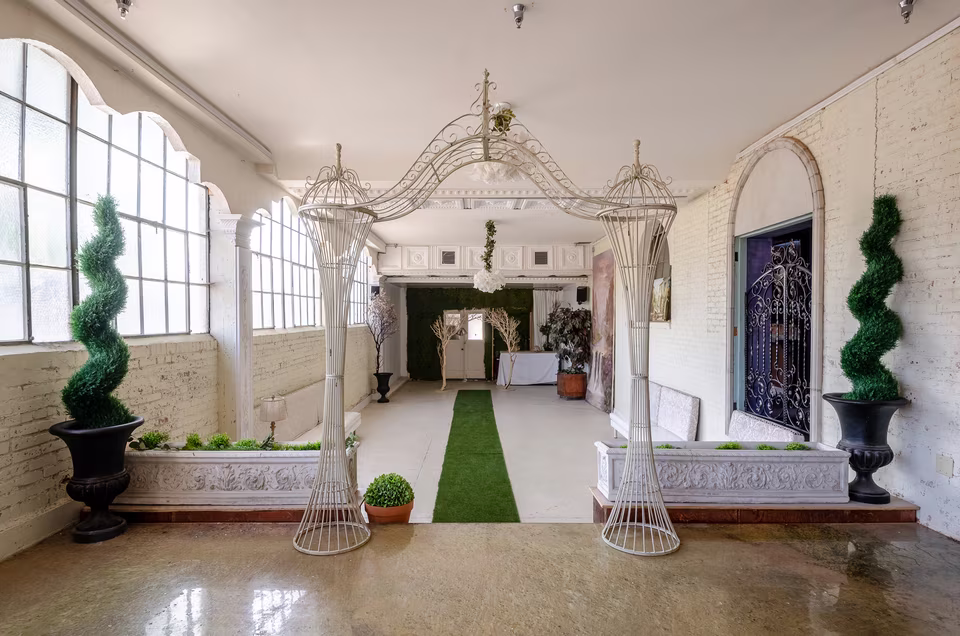 Centered view toward the raised platform in the white event room, with tall windows and sculptural arch frames.