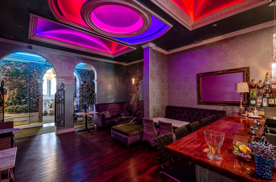 Reverse view across the wine lounge bar toward arched openings, colored ceiling light, and plush seating.