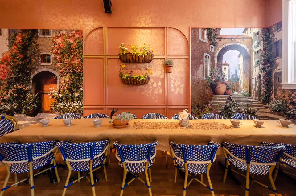 Colorful bistro dining room with a long communal table, blue woven chairs, peach walls, and garden murals.