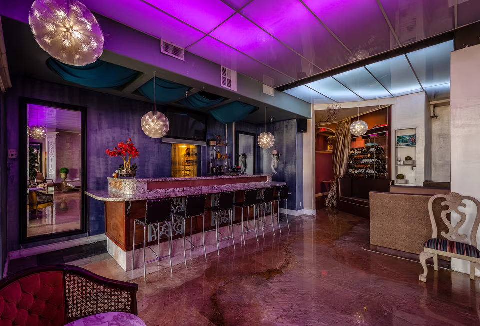 Purple-lit bar area with a long counter, hanging globe lights, and adjacent lounge seating.