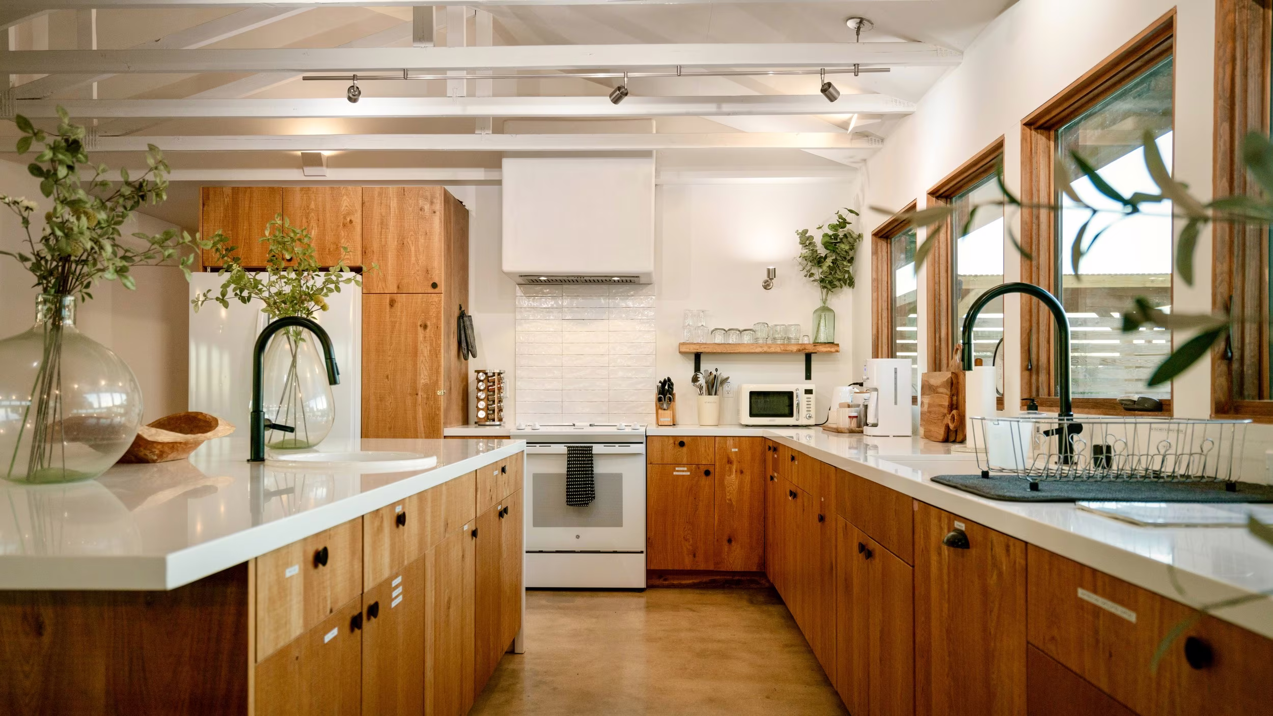 Compact kitchen with warm wood cabinets, white counters, black fixtures, and a tiled backsplash.