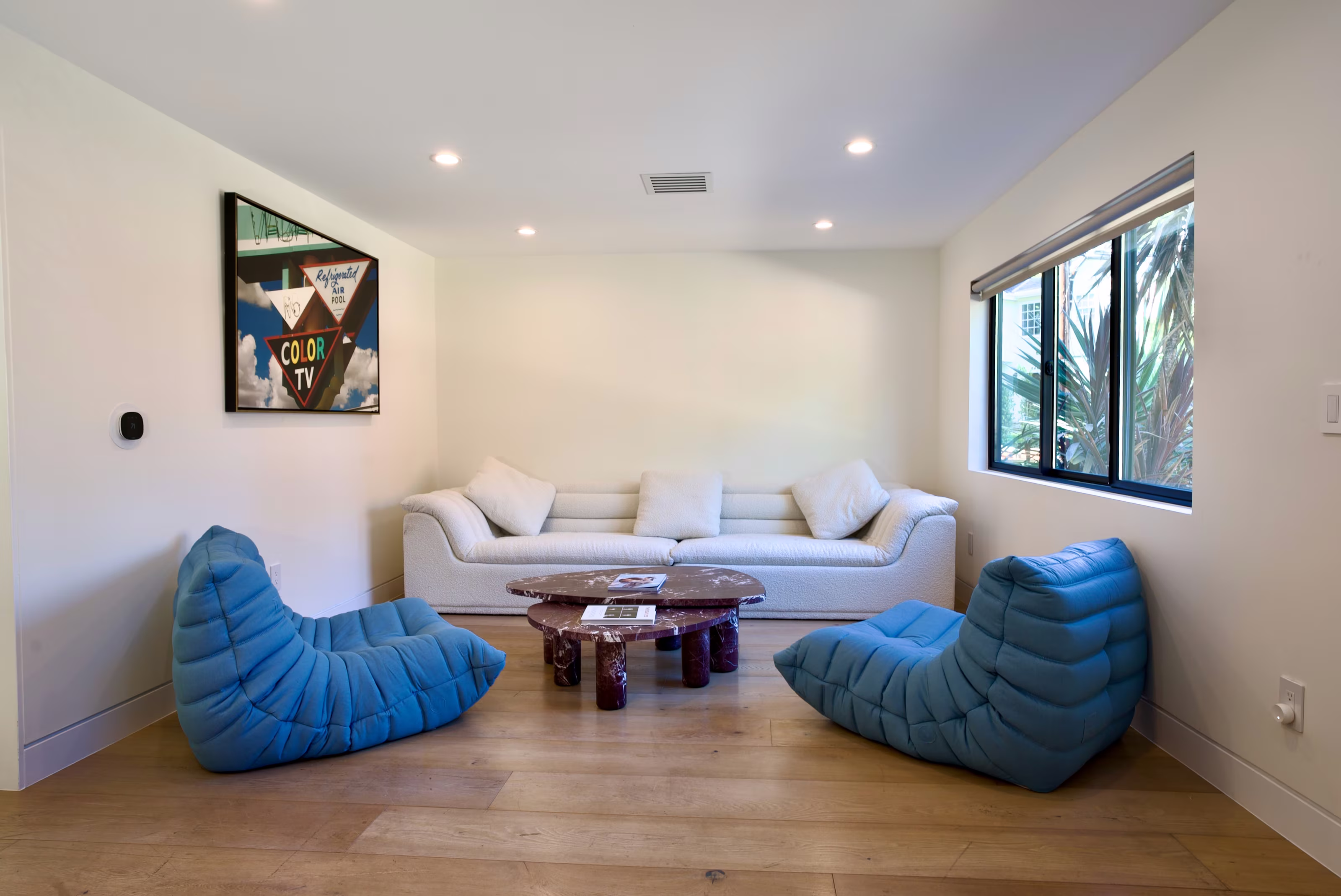 White entry lounge with three blue floor chairs, a cream sofa, and a round wood coffee table.