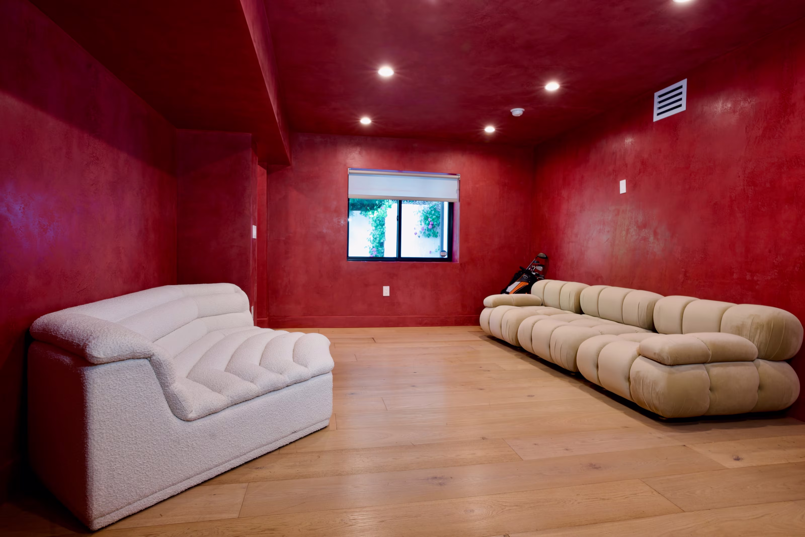 Red-walled entertainment room with pale wood floors and two curved cream sofas.