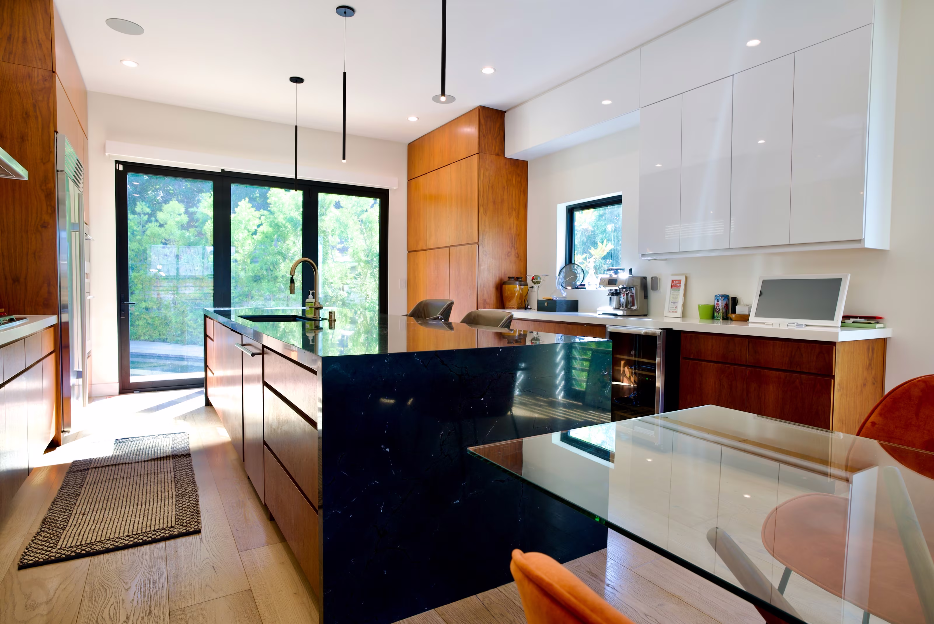 Modern kitchen with glossy white cabinets, wood panels, black stone island, and garden doors.