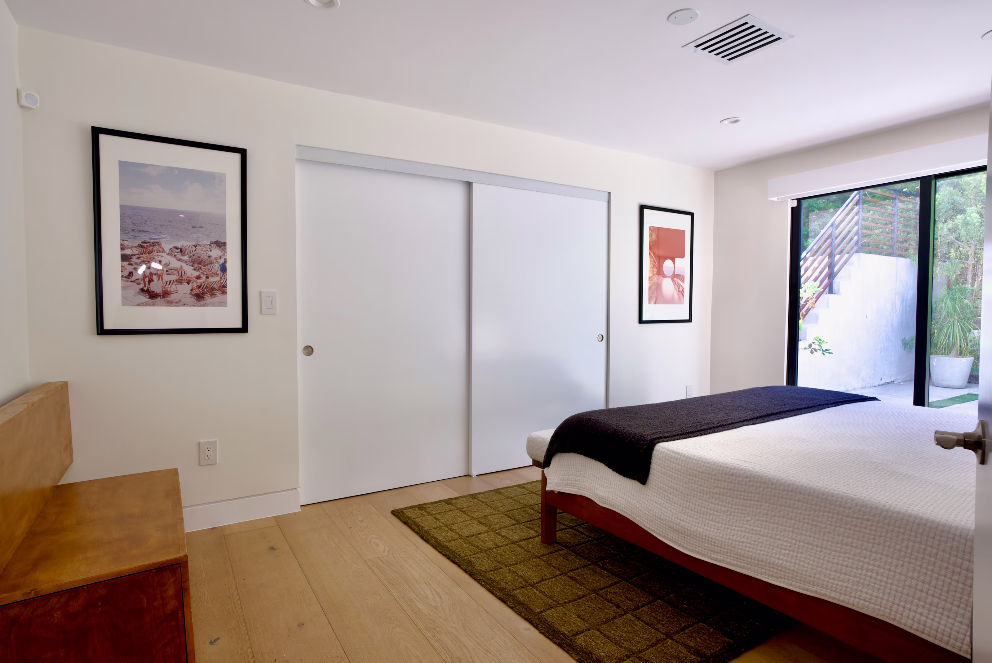 Guest bedroom with white sliding closet doors, low wood bed, framed art, and garden-facing glass doors.