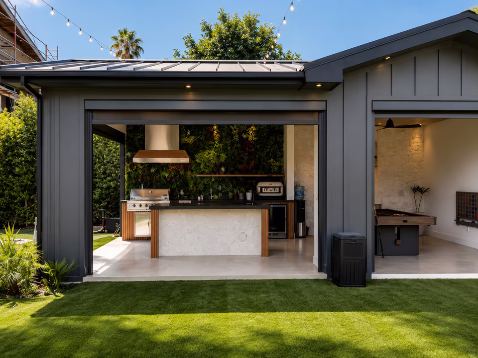 Covered outdoor kitchen with a built-in grill, stone counters, bar seating, and the pool visible beyond.
