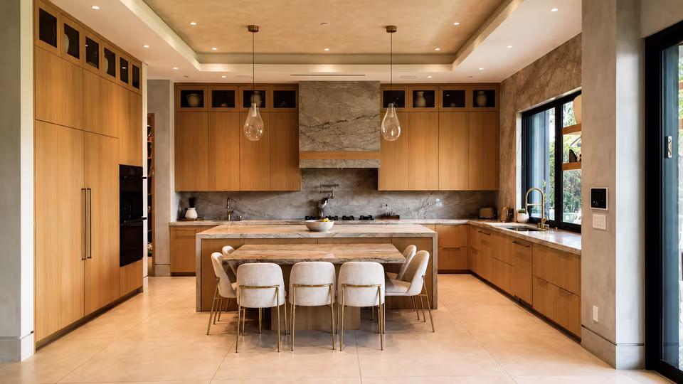 Open chef-style kitchen with a large waterfall island, wood cabinetry, pendant lights, and stainless appliances.