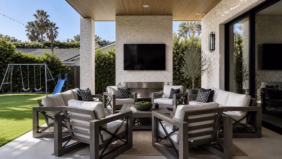 Covered outdoor lounge with sofas, dining furniture, ceiling fans, and an open view toward the pool.