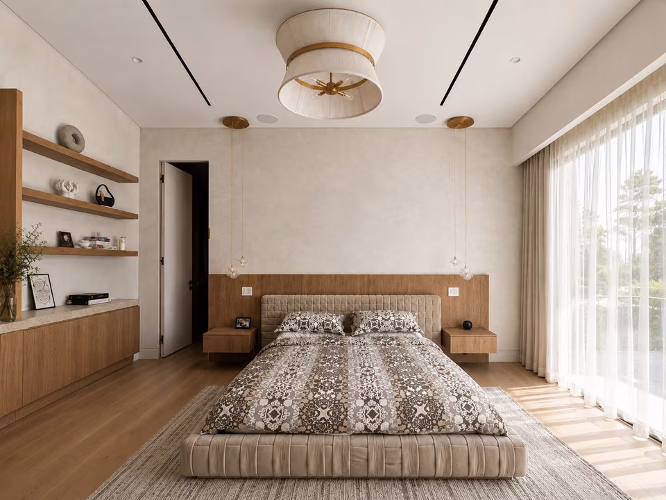 Wide primary bedroom with an upholstered bed, lounge seating, a fireplace wall, and glass doors to a balcony.