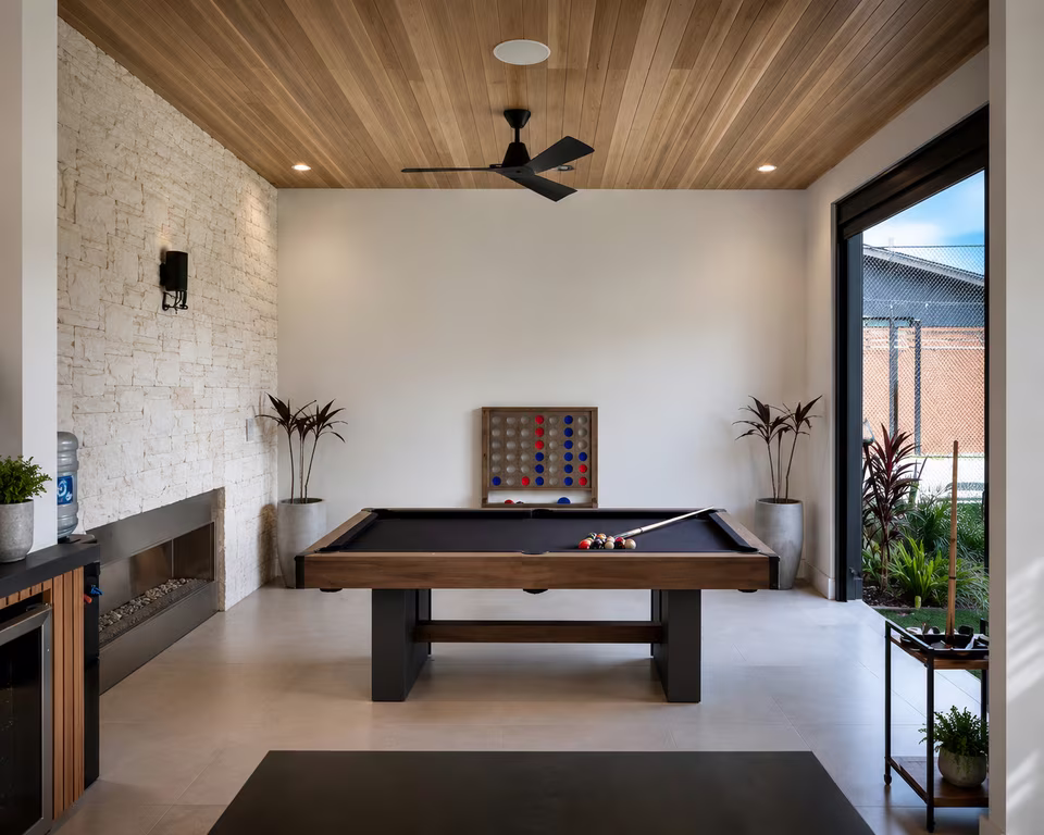 Game room with a billiards table, seating, wall-mounted screen, built-in storage, and warm wood flooring.
