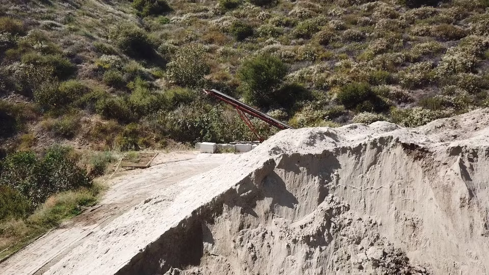 Close landscape view of a steep cut bank with stratified earth, rock texture, and a dirt work lane below.