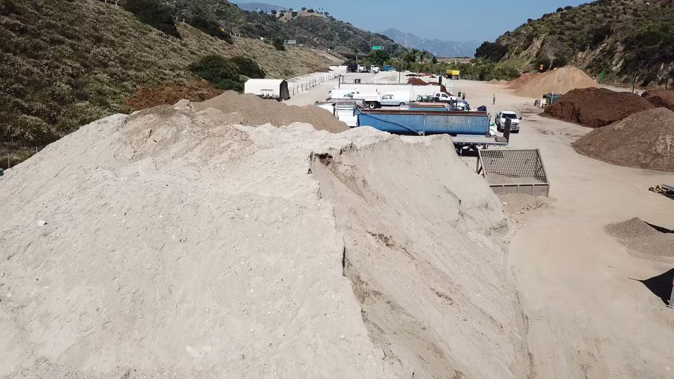 Elevated reverse view across the working yard, showing long dirt lanes, material piles, machinery, and distant vehicles.
